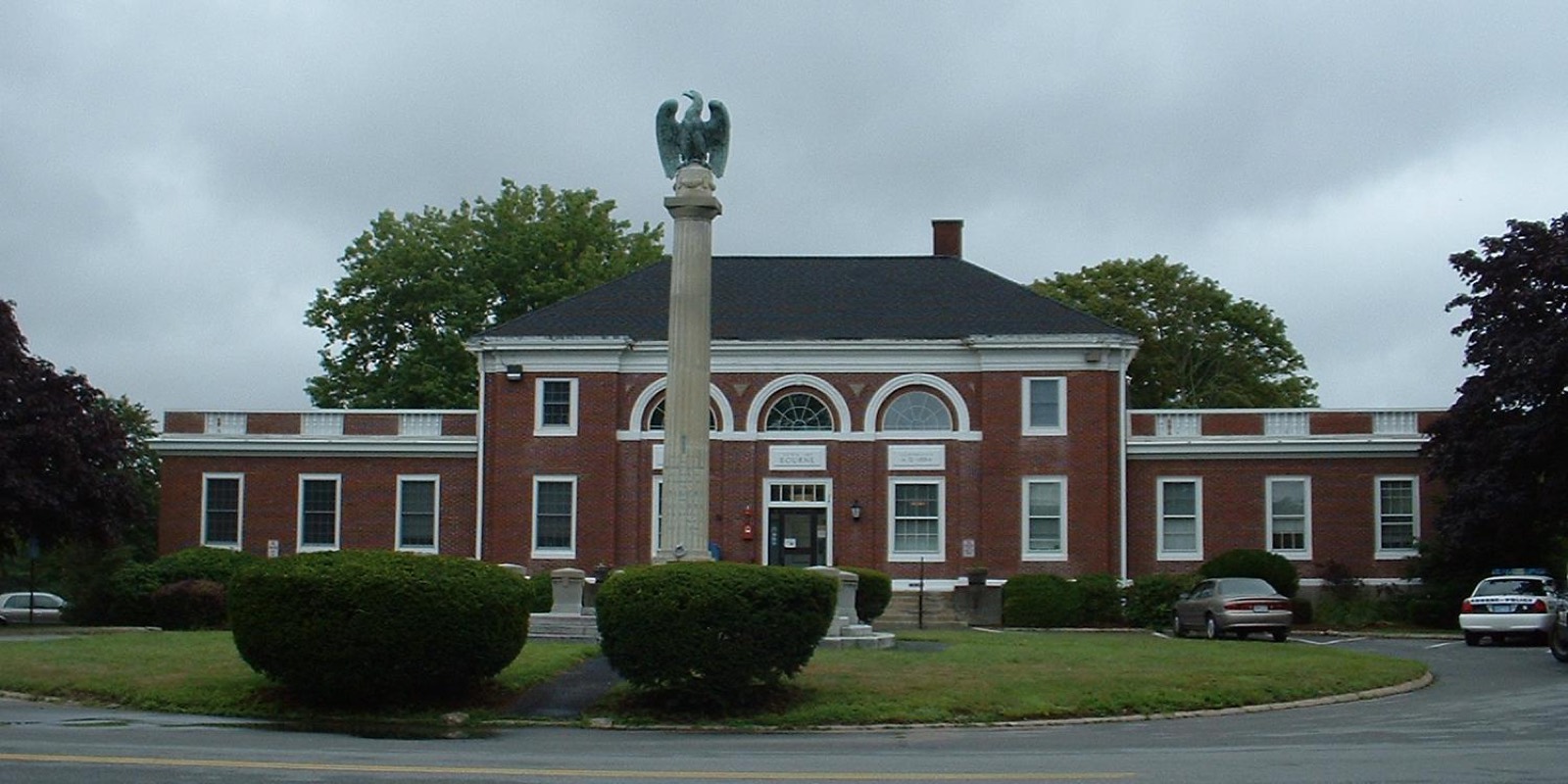 Bourne Town Hall, a brick building with a memorial column and eagle statue in front.