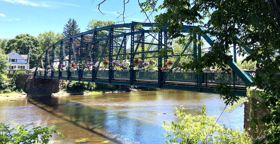 The green iron truss of the Old Drake Hill Flower Bridge over the Farmington River, with flower boxes along the railings